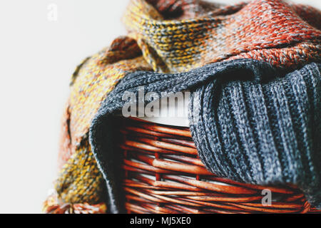 Stack of knitted winter scarfs on straw basket isolated on white background. Stock Photo