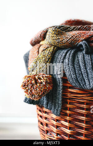 Stack of knitted winter scarfs on straw basket isolated on white background. Stock Photo