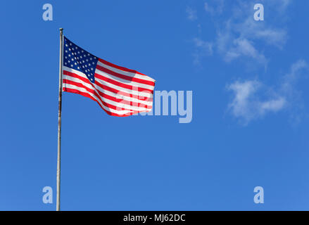 The American flag waves in the wind againts a blue sky. Stock Photo