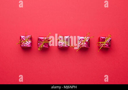 Small Red Christmas Gift Boxes organized in a row over red background, above view Stock Photo