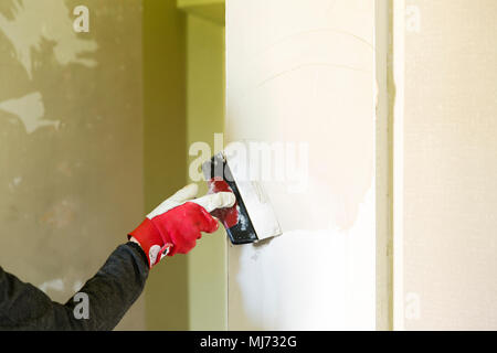 Plasterer home improvement handyman worker with putty knife working on apartment wall filling. Home renovation concept Stock Photo
