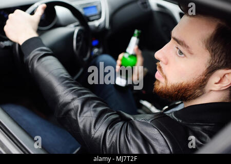 Drunk man with a bottle of beer driving a car Stock Photo