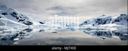 Panoramic view of snow covered mountains reflected on still water with cloudy sky, Paradise Habour, Antarctica Stock Photo