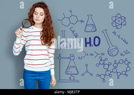 Serious chemist holding a magnifying glass while working in the laboratory Stock Photo