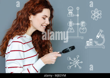 Positive laboratory worker smiling while using a magnifying glass Stock Photo