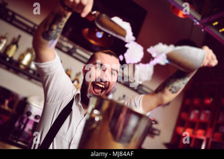 cheerful barman smiles, screams and falls asleep in a bucket for champagne on the background of the bar. Stock Photo