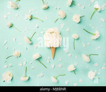 Waffle cone with white buttercup flowers over light blue background Stock Photo