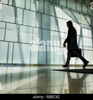 Silhouette of man carrying briefcase walking past glass wall. Stock Photo