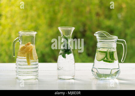 Three variants of fresh homemade lemonade with lemon, cucumber and mint. Lemonade in jugs and carafe on garden. Stock Photo