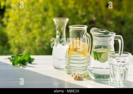 Three variants of fresh homemade lemonade with lemon, cucumber and mint. Lemonade in jugs and carafe on garden. Stock Photo