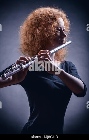 Young beautiful woman playing the flute on black background Stock Photo