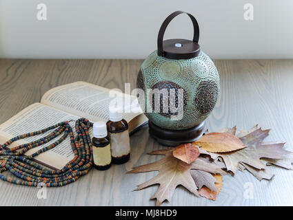 The ultrasonic aroma diffuser is made in the form of an old lamp. Aromatic diffuser is on the table. Near there are essential oils, a book, dry leaves Stock Photo