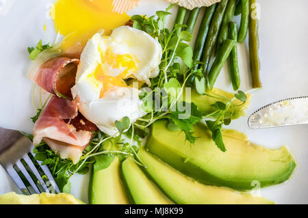 The poached egg in home with baby salad green beans and slices of avocado on a white plate Stock Photo