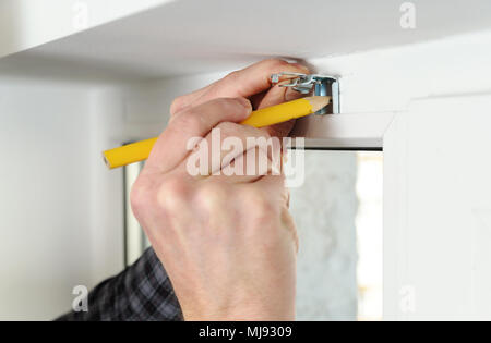 Installing wooden blinds. Man marks the place of mounting jalousie on the windows. Stock Photo