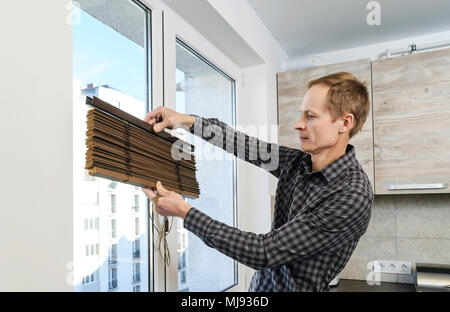 Installing wooden blinds. A man holds the folded jalousie. Stock Photo