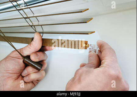 Installing wooden blinds. Man attaches the plastic braket to the bottom plank. Stock Photo