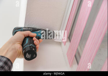 Installing fabric roller blinds. A man drilling holes to fix basis blinds. Stock Photo