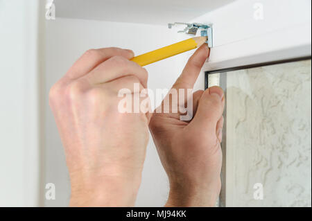 Installing wooden blinds. Man marks the place of mounting jalousie on the windows. Stock Photo