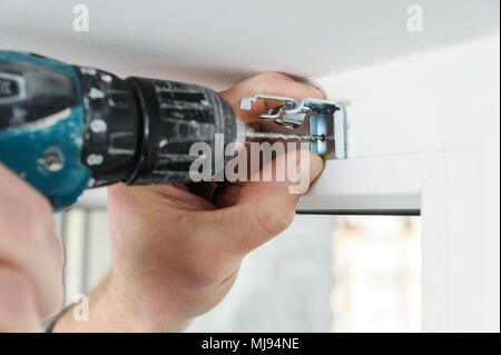 Installing wooden blinds. A man drill hole for fastening metal bracket that holds the jalousie. Stock Photo