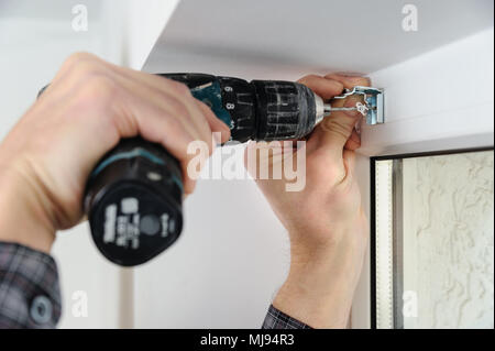Installing wooden blinds. A man drill hole for fastening metal bracket that holds the jalousie. Stock Photo