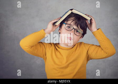 sad and pensive boy with a book on his head on gray background