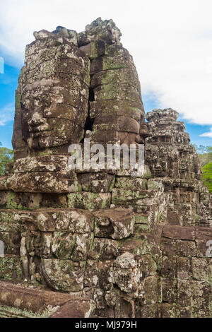 Ancient face sculptures on a tower of the unique Bayon temple in Angkor, Cambodia. In the background is another tower with stone faces visible. Stock Photo