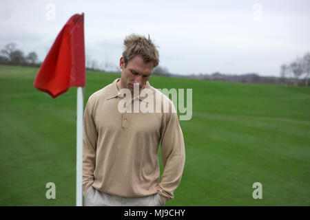 Amateur golf you mid 20's man waits at red flag on gold course. Stock Photo