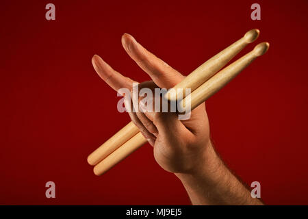 Man hand holding two drumsticks with devil horns rock metal gesture sign over red background, side view Stock Photo