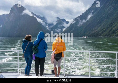 Milford sound New Zealand Milford sound three friends stood at the prow of an excursion boat returning from a boat trip on milford sound  South Island Stock Photo