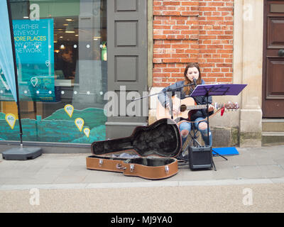 Abergavenny, Wales, UK: April 04, 2017: Busker in Abergavenny Town centre, street singer and guitar player young lady, who was singing in a public pla Stock Photo