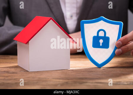 Close-up Of A Businessperson's Hand Holding Shield Security Icon Besides House Model Stock Photo