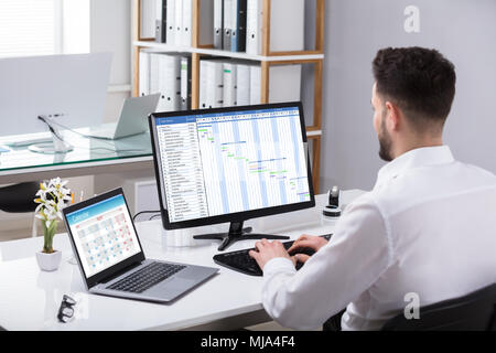Businessman Analyzing Gantt Chart On Computer With Laptop Over Desk Stock Photo