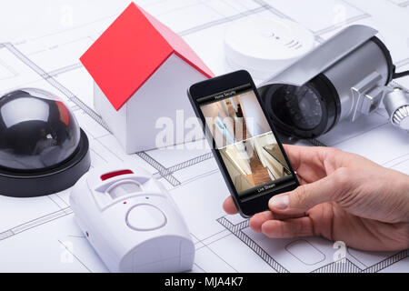 Architect Using Home Security System On Mobile Phone Near Security Equipments And House Model Stock Photo