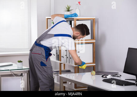 Close-up Of A Young Male Cleaner Cleaning Shelf At Workplace Stock Photo