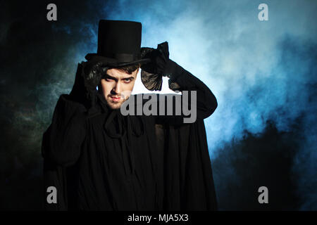 Man in a black top hat and cloak. Demonic image. Magician illusionist. Smoke background Stock Photo