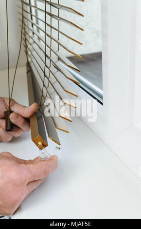 Installing wooden blinds. Man attaches the plastic braket to the bottom plank. Stock Photo