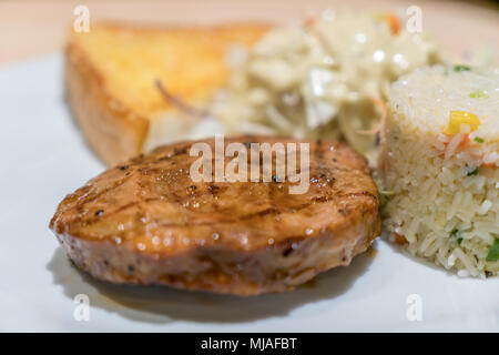 Pork steak with salad and rice on white dish in restaurant. Stock Photo