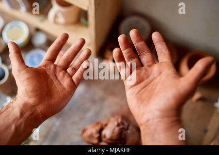 Mature male potter showing his palms while molding a clay in pottery workshop, close-up, selective focus. Creative work process. Craftsman preparation Stock Photo