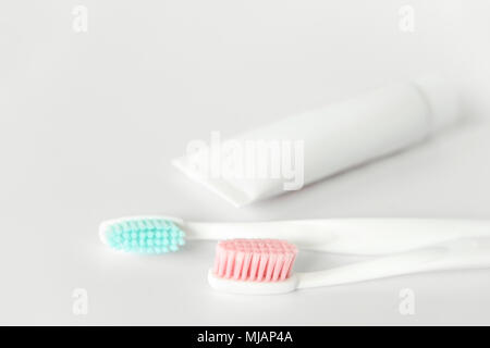 Close up of two plastic white toothbrushes with pink and blue bristle and toothpaste in tube on white background. Stock Photo