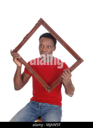 Scared looking African American man holding up a picture frame in a red t-shirt, isolated for white background Stock Photo