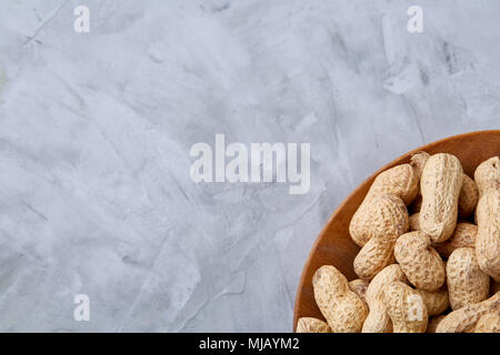 Unpeeled peanuts in wooden bowl over white textured background closeup, selective focus. Healthful and nutritious snack. Delicious ingredient for your Stock Photo
