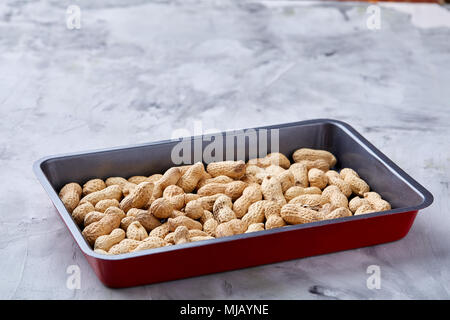 Unpeeled raw peanut on baking tray over white textured background, selective focus, shallow depth of field. Ready to bake. Healthful and nutritious sn Stock Photo