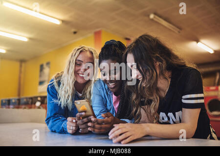Smiling young female friends leaning on a laundromat counter using a cellphone while doing laundry together Stock Photo