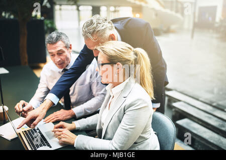 Mature manager and two work colleagues discussing business together on a laptop during a meeting in the lobby of an office building Stock Photo