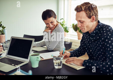 Two smiling young business colleagues sitting together at a table in an office going over paperwork Stock Photo