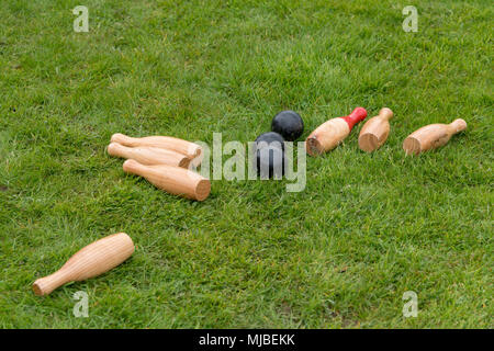 set of fallen traditional wooden skittles outdoors on grass with black balls in summer in UK Stock Photo