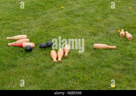 set of fallen traditional wooden skittles outdoors on grass with black balls in summer in UK Stock Photo
