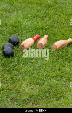 set of fallen traditional wooden skittles outdoors on grass with black balls in summer in UK Stock Photo