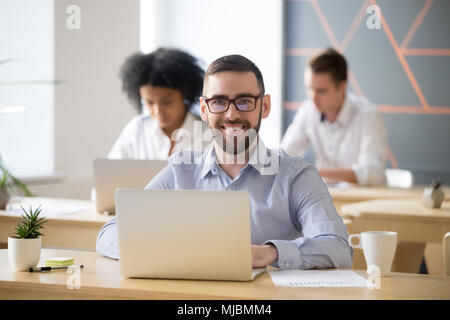 Smiling businessman sitting at desk with laptop in office, portr Stock Photo