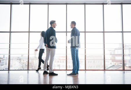Two businessmen deep in discussion together while standing in an office boardroom with windows overlooking the city. Stock Photo